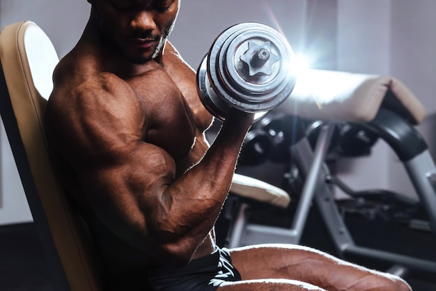 Male athlete lifts the dumbbell biceps in the gym