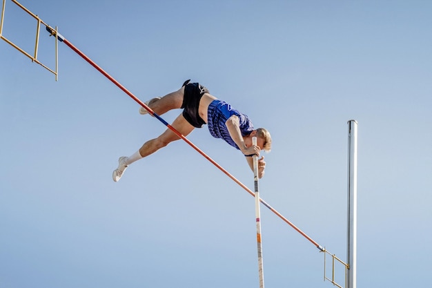 Foto atleta maschile che salta con il palo sullo sfondo blu del cielo
