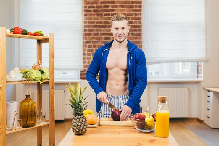 Photo male athlete prepares salad and fresh fruit juice at home in the kitchen