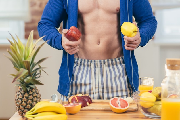 Спортсмен-мужчина готовит салат и свежий фруктовый сок дома на кухне
