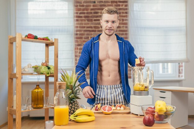 Male athlete prepares salad and fresh fruit juice at home in the kitchen