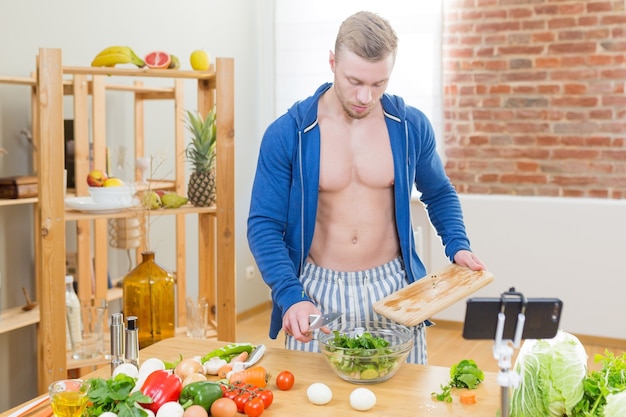 Atleta maschio che prepara cibo sano a casa in cucina, studiando online