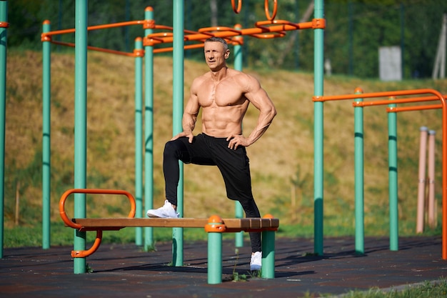 Male athlete with bare torso stretching legs outdoors