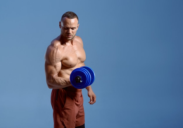 Male athlete with dumbbells poses in studio