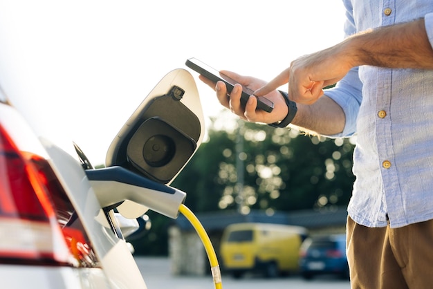 電気自動車を差し込むスマートフォンの男性のアプリを使用して電気自動車に電源コードを接続する男性