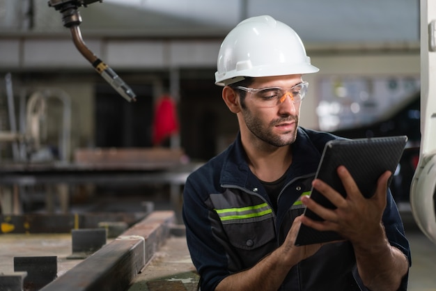 産業工場でタブレット制御ロボットアーム溶接機を使用する男性の自動化エンジニア