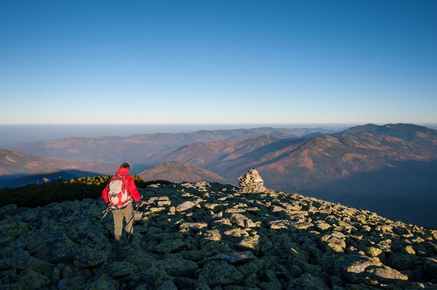 Photo male backpaker walking on the rocky top of the mountain