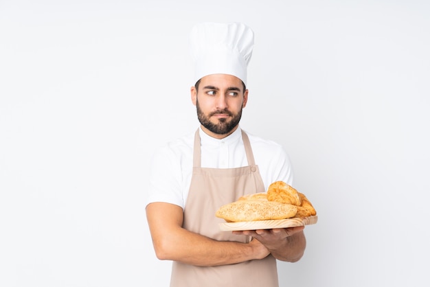 Мужской пекарь держит стол с несколькими хлебами на белой стене, думая идею