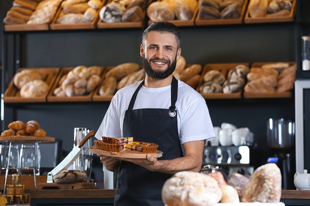 Panettiere maschio che tiene tavola di legno con deliziosa torta al chiuso