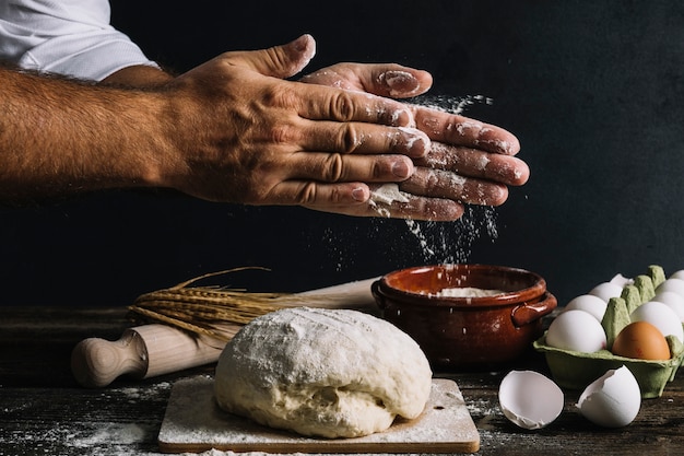 Male baker's hand dusting flour on knead dough