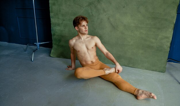 Male ballet dancer sittiing on the floor in dancing class, grunge wall on background