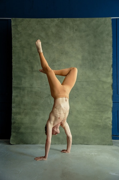 Male ballet dancer standing on hands, grunge wall on background, dancing studio