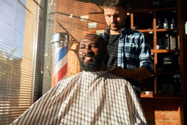 Male barber putting cape on client at barbershop