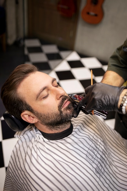 Парикмахер стрижет бороду своего клиента