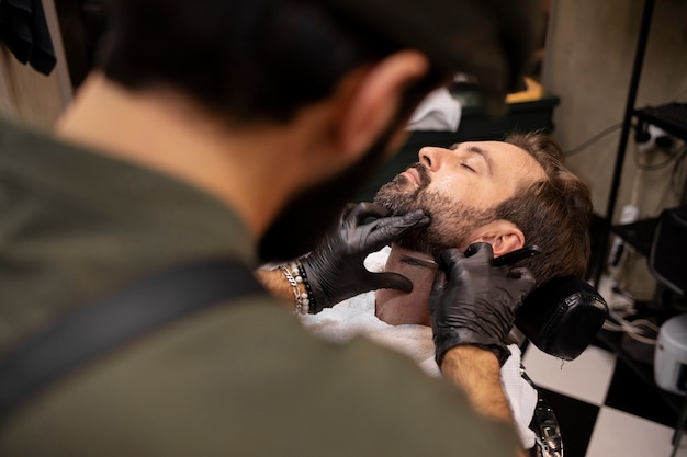 Photo male barber trimming his client's beard