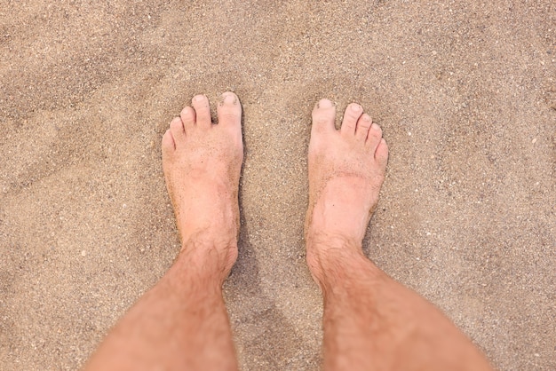 Male bare feet on hot beach sand closeup