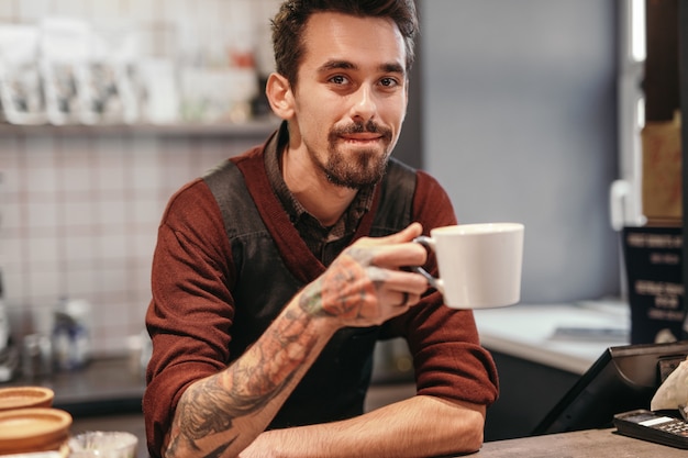 Male barista drinking hot beverage in cafe