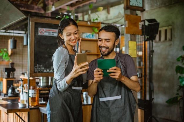 Male barista holding the deposit book while looking at the phone that holded by the female barista