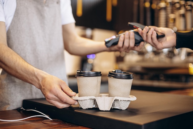 Male barista holding terminal while customer paying with card