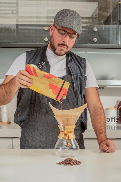 Male barista is making black coffee in chemex coffee maker, standing in front of coffee shop bar