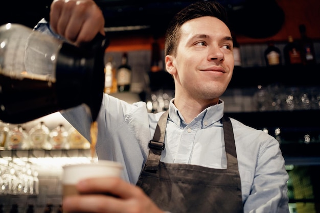 A male barista makes a takeaway coffee clothing apron uniform\
of the bar staff