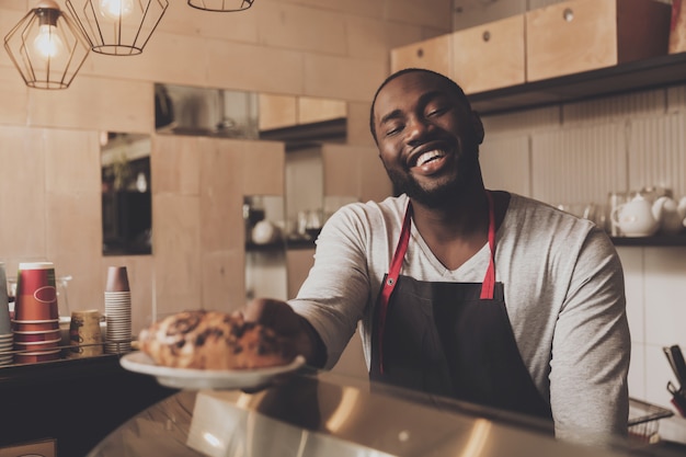 Male barista serves a croissant ordered to client