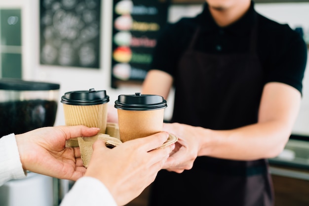 コーヒーショップで持ち帰り用の紙の使い捨てカップでコーヒーを提供する男性のバリスタ。