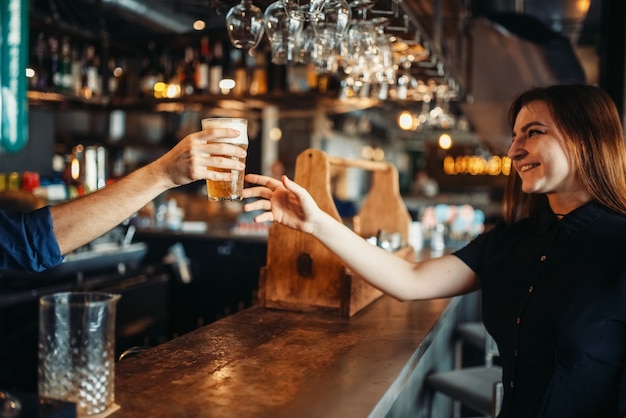 Male barman passes glass of beer to female visitor