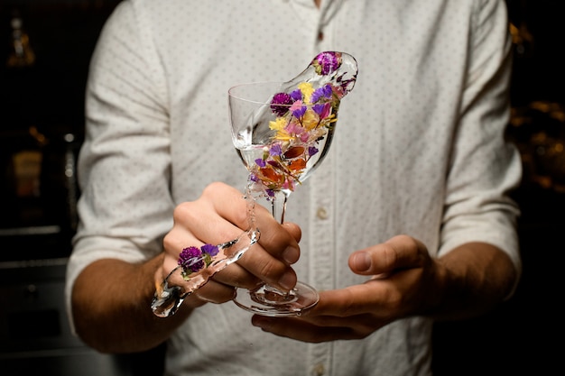 Мужской бармен делает выплеск с коктейлем в бокале, украшенном цветами