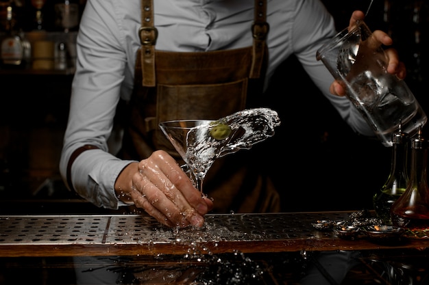 Male bartender mixing an alcoholic drink in the martini glass with one olive