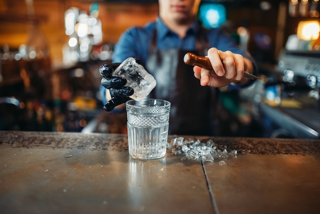 Male bartender pours a drink into a glass with ice