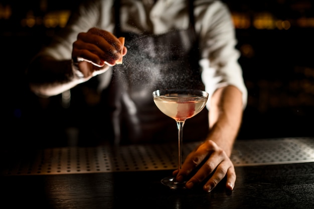 Male bartender serving a cocktail in the glass decorated with pink ice cube