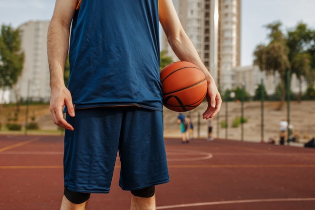 Male basketball player holds a ball on outdoor court.