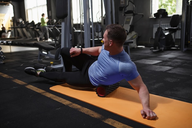 Culturista maschio che si allunga in palestra usando il rullo di schiuma