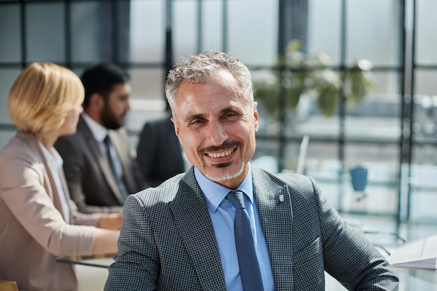 male boss against the background of her colleagues looks at the camera in a modern office