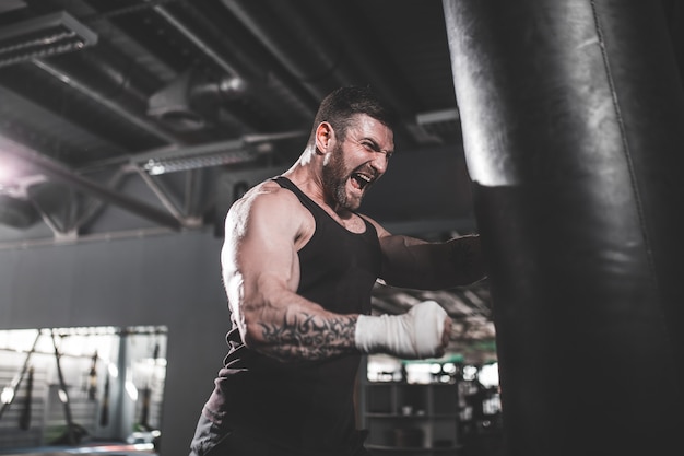 Тренировка мужского боксера с грушей в темной спортивной зале.