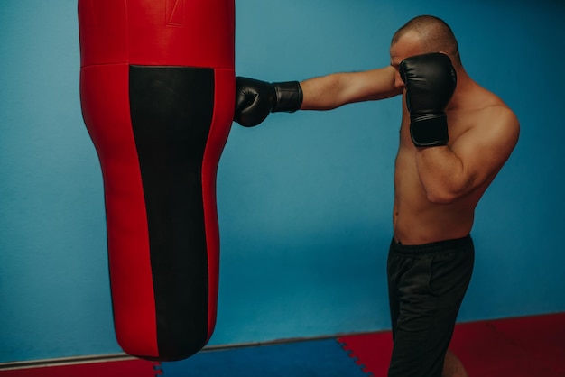 Male boxer training with punching bag in dark sports hallMale boxer as exercise for the big fight Boxer hits punching bag