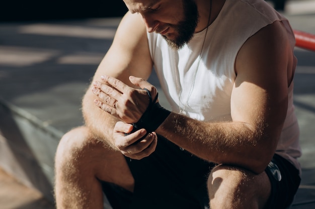 Male boxer wraps his hands with black handwrap before the fight training