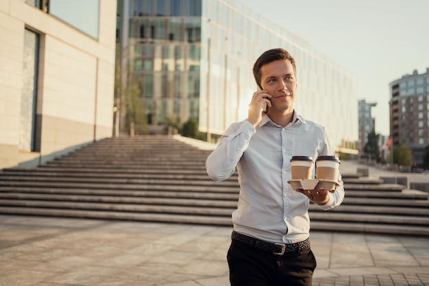 Male break manager carries coffee to the office and talks on\
the phone