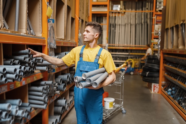 Photo male builder choosing piping at the shelf in hardware store. constructor in uniform look at the goods in diy shop