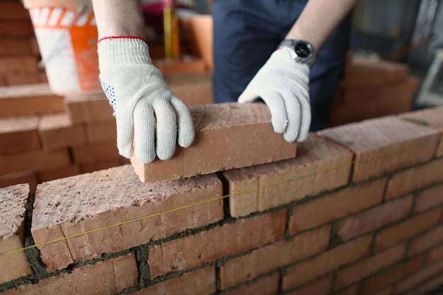 Male builder hands making make brickwork using red bricks