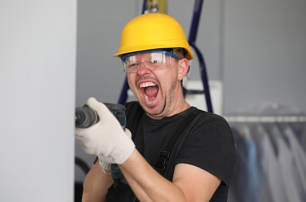 Male builder in helmet drills wall and screams