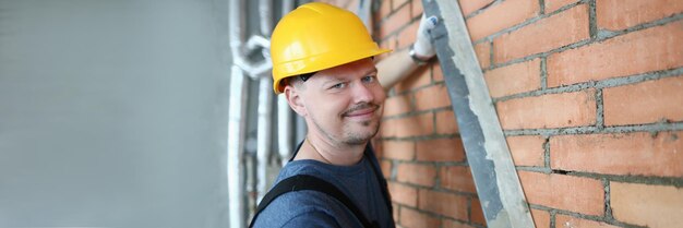 Мужчина-строитель изготавливает кирпич из стен и держит рабочий инструмент