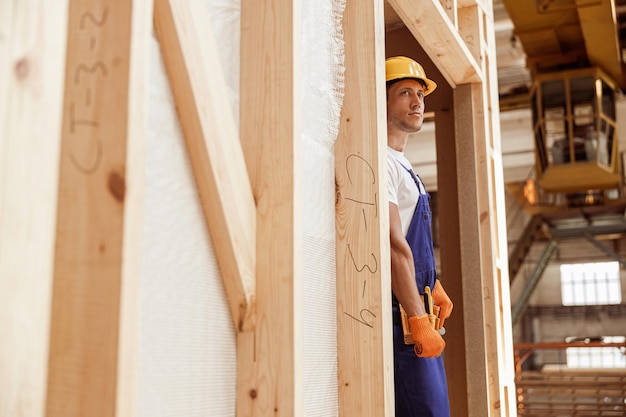 Male builder standing in doorway of wooden construction cabin