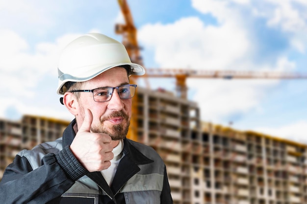 A male builder in a white hard hat against a blurred background of a construction site with a blue sky Positive civil engineer with a beard