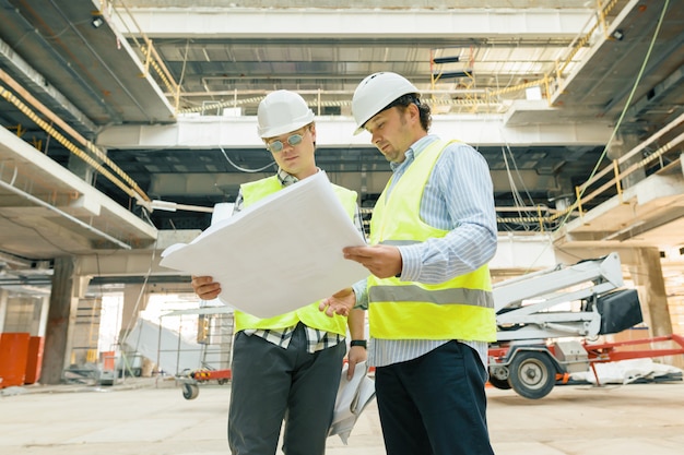 Male building workers working at construction site, builders looking in blueprint