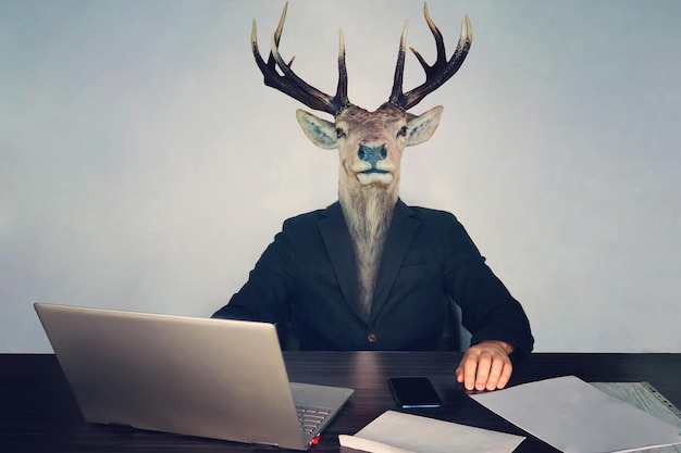 Male business man with deer head on a blue background in the office at the Desk concept of irrational management stupid employees and employees in the company and morons deputies in the government