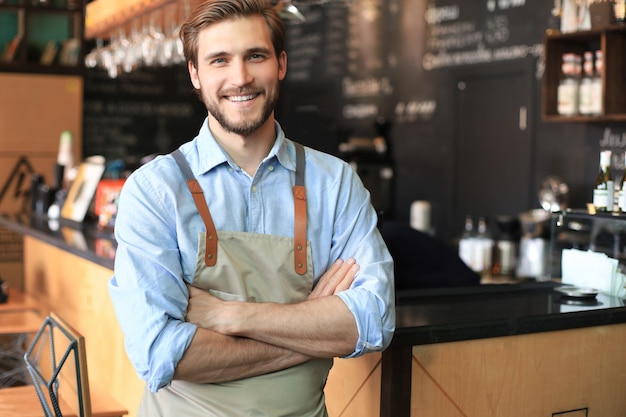 カメラを見ながら、腕を組んで喫茶店のカウンターの後ろに男性経営者。