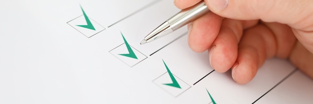 Male businessman hand hold silver pen and make green check mark closeup