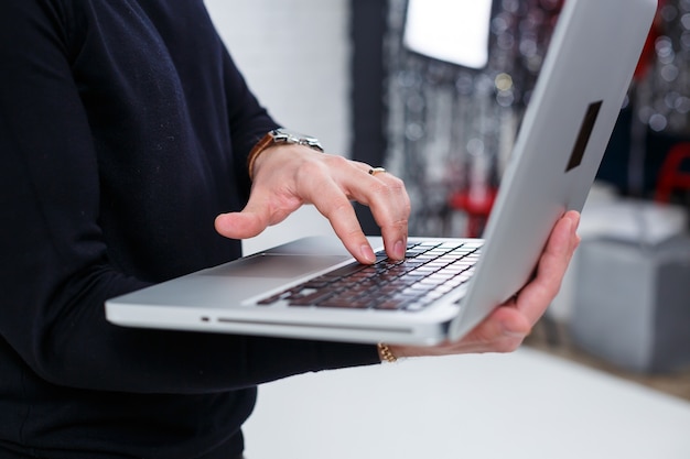 A male businessman manager smiles and stands with a laptop in his hands and looks at the screen. Stands on a white background.